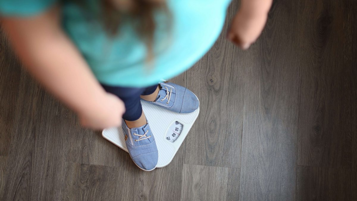 As consequências da obesidade em uma menina com excesso de peso em pé em uma balança